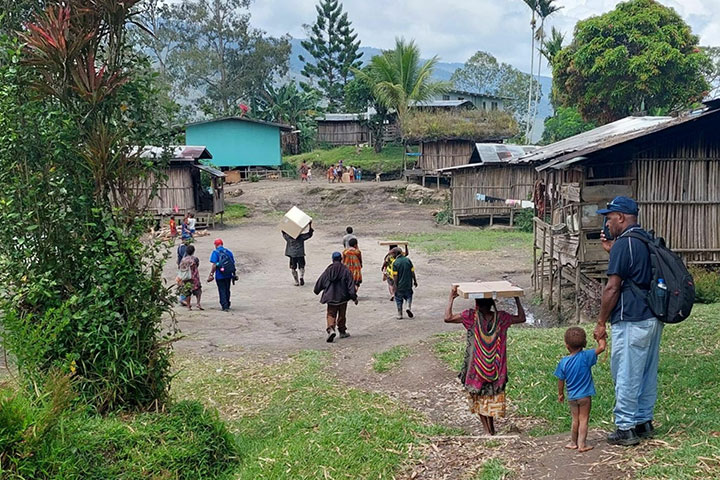 Vue d'un village où des personnes marchent en portant des kits de panneaux solaires sur la tête