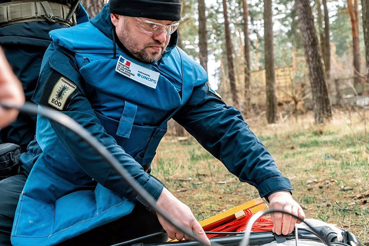 Un homme portant une uniforme de démineur en train de décontaminer une terre